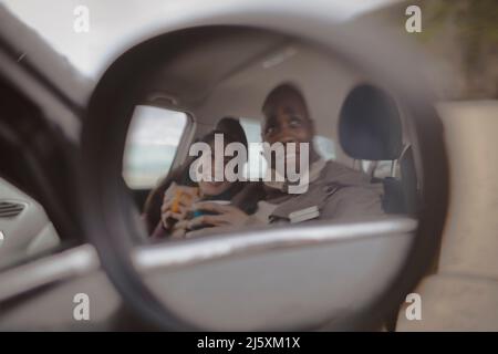 Spiegelung des glücklichen Paares, das Kaffee im Auto trinkt, Seitenspiegel Stockfoto