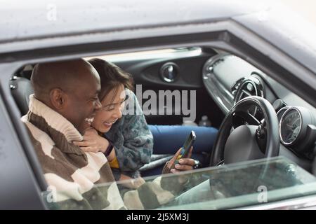 Glückliches Paar, das Smartphone im Autofenster benutzt Stockfoto