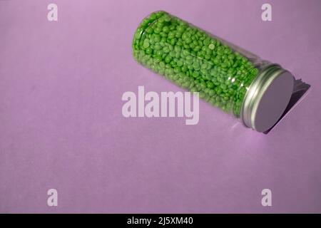 Grünes Wachs zur Enthaarung in Granulat. Auf violettem Hintergrund. Glas mit Wachs auf isoliertem Hintergrund Stockfoto