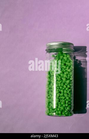 Grünes Wachs zur Enthaarung in Granulat. Auf violettem Hintergrund. Glas mit Wachs auf isoliertem Hintergrund. Stockfoto