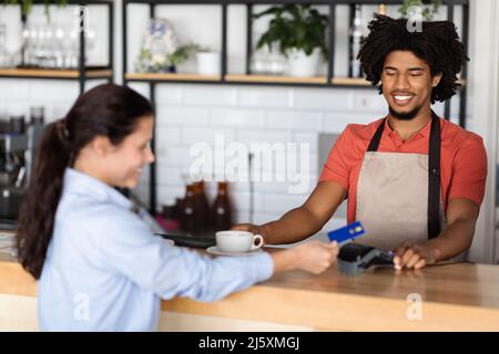Happy Millennial african american Curly männlichen Kellner im Vorfeld gibt frischen Kaffee an Kunden Stockfoto