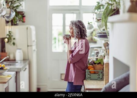 Nachdenkliche ältere Frau trinkt Kaffee in der Küche Stockfoto