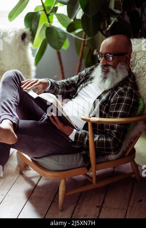 Reifer Mann mit Bart Lesebuch im Sessel Stockfoto