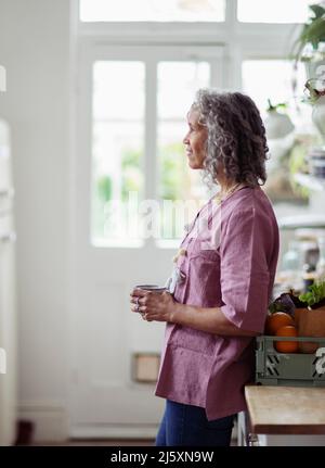 Nachdenkliche ältere Frau, die zu Hause Kaffee trinkt Stockfoto