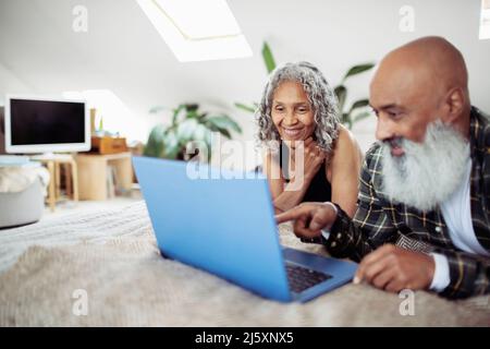 Glückliches Ehepaar mit Laptop im Bett Stockfoto