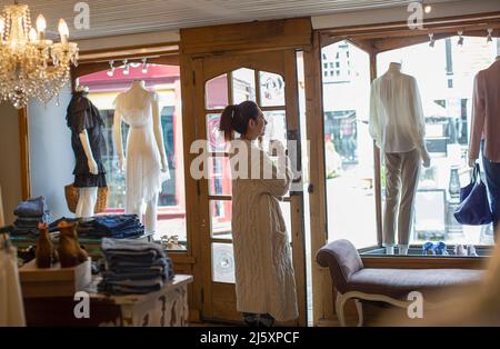 Weibliche Boutique-Besitzerin trinkt Kaffee am Schaufenster Stockfoto