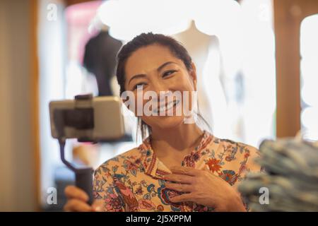 Lächelnde weibliche Ladenbesitzerin vloggt mit Smartphone und Selfie-Stick Stockfoto