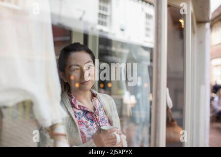 Weibliche Geschäftsbesitzerin trinkt Tee am Schaufenster Stockfoto