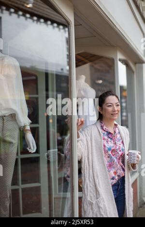 Selbstbewusste Geschäftsbesitzerin, die vor der Boutique Tee trinkt Stockfoto