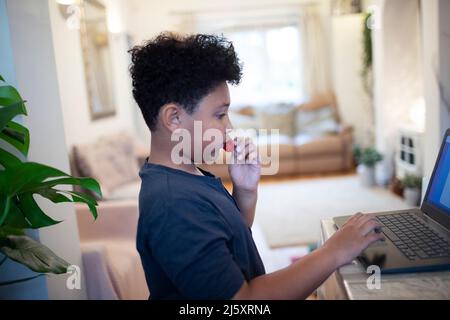 Junge, der zu Hause am Laptop Erdbeeren isst Stockfoto