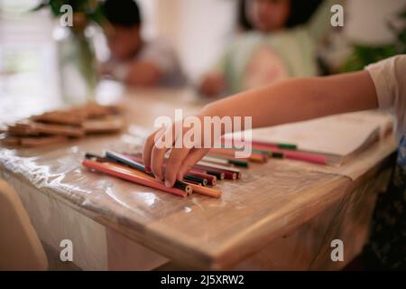 Mädchen, das nach Buntstift auf dem Tisch greift Stockfoto