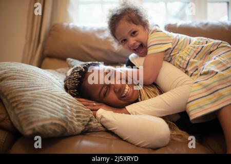 Glückliche verspielte Mutter und Tochter auf dem Sofa Stockfoto