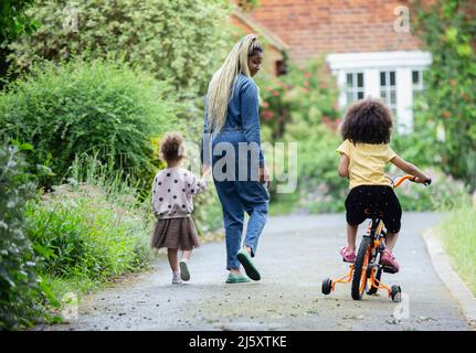 Mutter und Töchter gehen und reiten Fahrrad in der Auffahrt Stockfoto