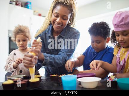 Glückliche Mutter und Kinder dekorieren Cupcakes in der Küche Stockfoto