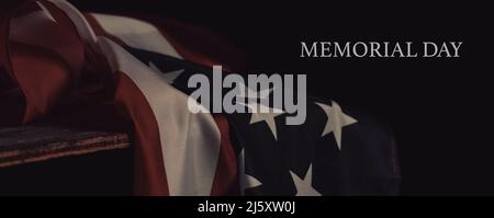 Der Text Memorial Day und die amerikanische Flagge, die auf einer Oberfläche, mit einer dramatischen Beleuchtung, vor einem schwarzen Hintergrund, in einem Panorama-Format als zu verwenden Stockfoto