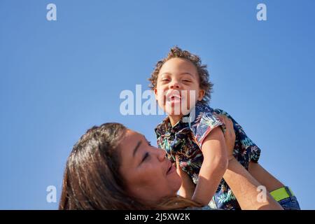 Portrait Mutter hebt glücklichen, sorglosen Sohn mit Down-Syndrom Stockfoto