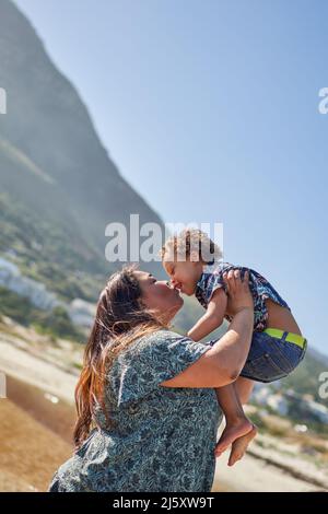 Glückliche, liebevolle Mutter küsst Sohn am sonnigen Strand Stockfoto