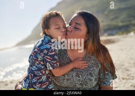 Glückliche, liebevolle Mutter und Sohn küssen sich am sonnigen Strand Stockfoto