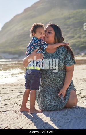 Liebevolle Mutter umarmt glücklichen Sohn am sonnigen Strand Stockfoto