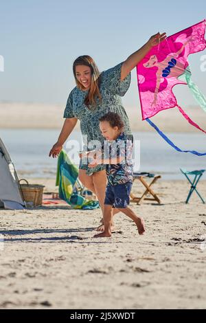 Glückliche Mutter und Sohn spielen mit Drachen am sonnigen Strand Stockfoto