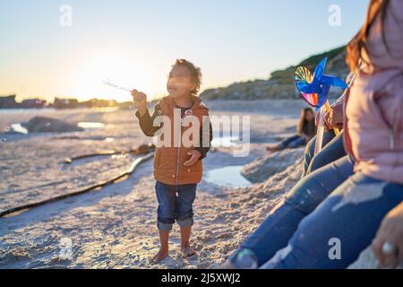 Netter Junge mit Down-Syndrom, der am sonnigen Strand mit Blasen spielt Stockfoto