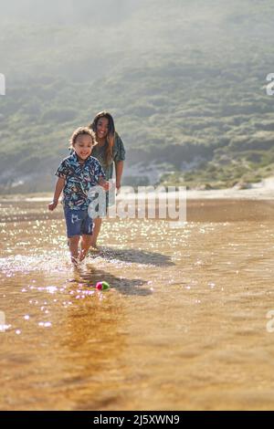 Glückliche Mutter und Sohn spielen mit Ball in der Meeresbrandung Stockfoto