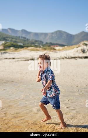 Glücklicher Junge mit Down-Syndrom, der am sonnigen Strand spielt Stockfoto