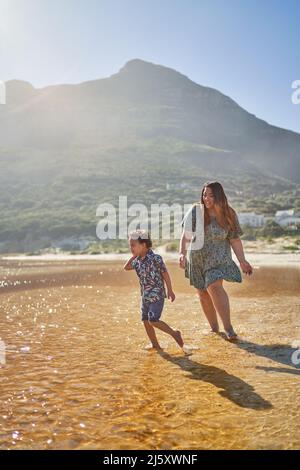 Mutter jagt Sohn in sonniger Meeresbrandung Stockfoto