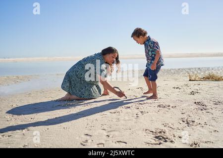 Mutter und Sohn mit Down-Syndrom ziehen im Sand mit Stock am Strand Stockfoto