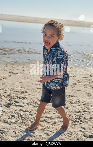 Portrait glücklicher Junge mit Down-Syndrom am sonnigen Strand Stockfoto