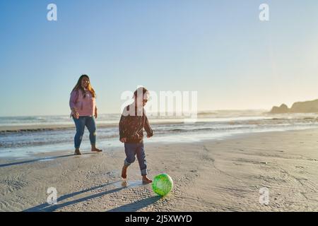 Mutter und Sohn mit Down-Syndrom spielen am Strand mit Fußball Stockfoto