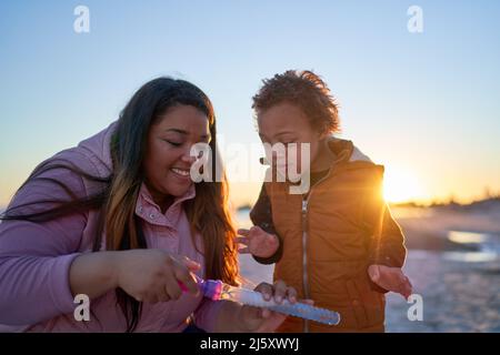 Glückliche Mutter und Sohn mit Down-Syndrom spielen mit Blasen am Strand Stockfoto