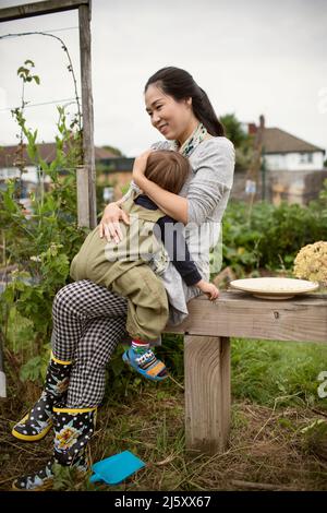 Glückliche Mutter hält müde Kleinkind Sohn auf Bank im Garten Stockfoto