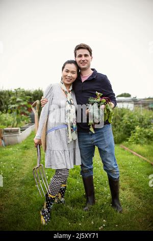 Portrait glückliches Paar mit geerntetem Gemüse im Garten Stockfoto