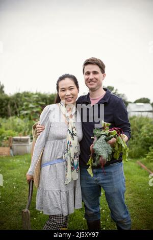 Portrait glückliches Paar mit geernteten Rüben im Garten Stockfoto