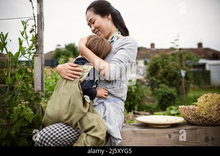 Glückliche Mutter hält Kleinkind Sohn auf Gartenbank Stockfoto