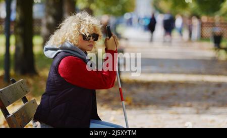 Junge blonde blinde Frau im Park in einer Brille mit einem Stock Stock Medium Schuss Kopie Raum Herbst Park Hintergrund . Hochwertige Fotos Stockfoto