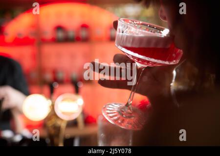 Nahaufnahme eines Gourmet-Mixed-Drink-Cocktails aus süßem rosafarbenem Limonade-Wodka und Gin martini, garniert von einer Zitronenscheibe und Stroh, auf einem Holzgrai Stockfoto