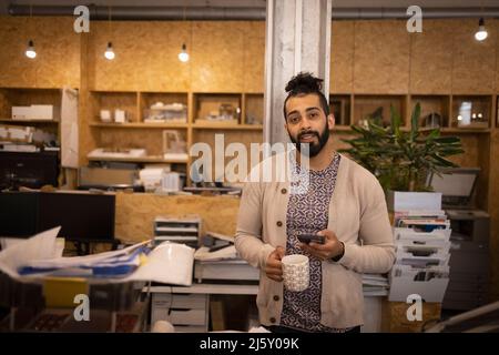 Portrait selbstbewusster junger männlicher Designer mit Kaffee und Telefon Stockfoto