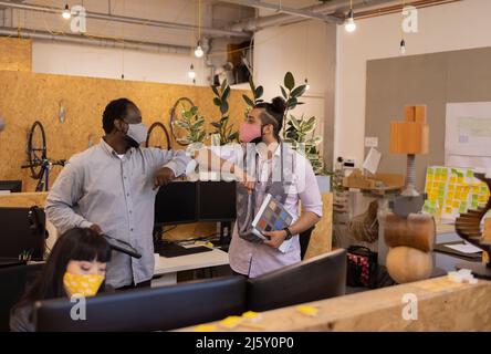 Geschäftsleute in Gesichtsmasken Ellbogen stoßen im Büro Stockfoto