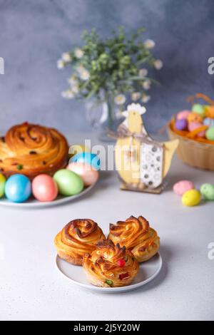 Craffin mini (Cruffin) mit Rosinen und kandierten Früchten. Traditionelles Osterbrot Kulich. Im Hintergrund ist ein großes Cruffin und bemalte Eier auf einem gr Stockfoto