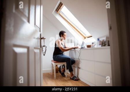 Reife Frau, die von zu Hause aus am Laptop im Schlafzimmer arbeitet Stockfoto