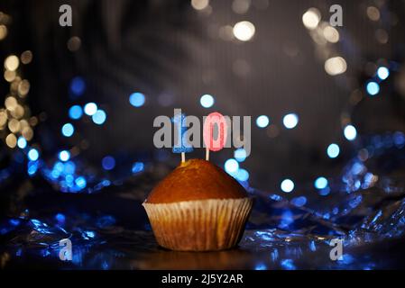 Hausgemachter leckerer Cupcake oder Muffin mit der Nummer 10 zehn auf dem Tisch mit Aluminiumfolie und verwackelten hellen Hintergrund. Geburtstag oder Jubiläum Grußkarte Konzept. Hochwertige Fotos Stockfoto