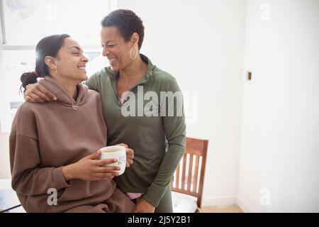 Glückliche Mutter und junge Erwachsene Tochter umarmen zu Hause Stockfoto
