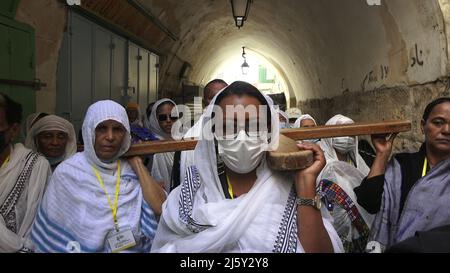 Äthiopisch-orthodoxe Christen tragen während der orthodoxen Karfreitagsprozession am 22. April 2022 in Jerusalem, Israel, ein großes Holzkreuz auf der Via Dolorosa. Juden, Christen und Muslime feiern in derselben Woche das diesjährige Passah, Ostern und den Ramadan. Stockfoto