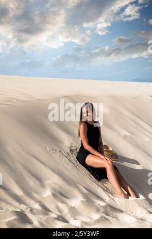 Attraktive junge islamische Frau in lässigem Hemd und dunklem Hijab Stehen auf rotem Hintergrund und Blick auf die Kamera Stockfoto