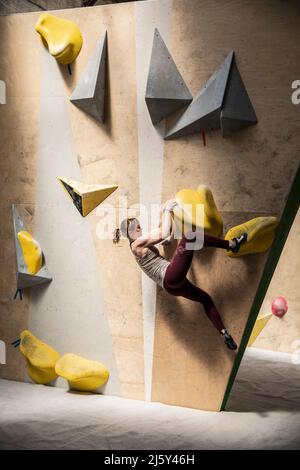 Junge Klettererin, die an der Kletterwand hängt Stockfoto
