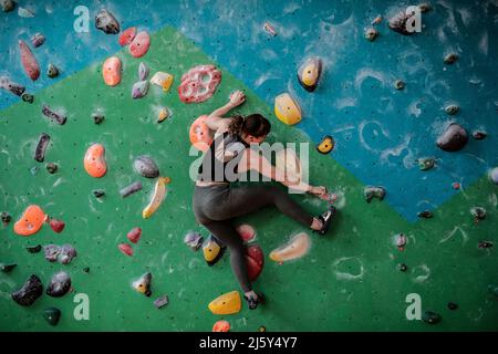 Weibliche Klettererin, die an der Kletterwand hängt Stockfoto