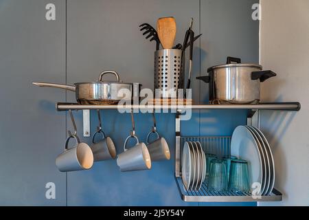 Regale mit verschiedenen Utensilien und Geschirr hängen an der Wand über dem Waschbecken in der hellen Küche der Wohnung Stockfoto