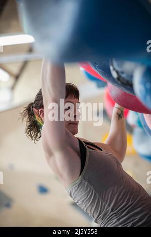 Junge Klettererin, die an der Felswand hängt Stockfoto